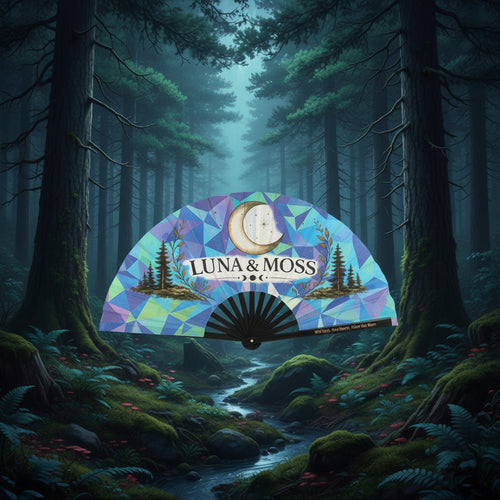Luna & Moss hand fan open showing geometric stained-glass design in blues, purples, and greens with pine tree logo